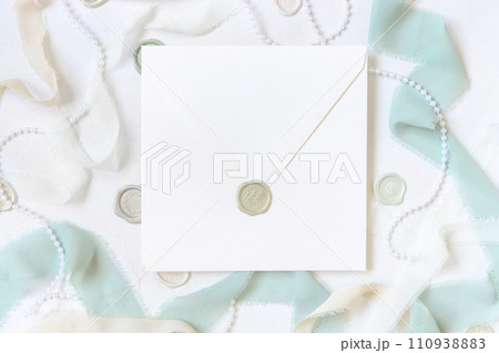 Envelope near light green and beige decorations and silk ribbons on white table top view, mockup Envelope near light green and beige decorations and silk ribbons on white table top view, mockup 110938883