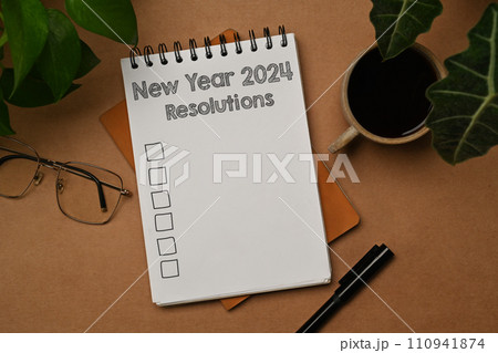 2024 New Year Resolutions text on a spiral notebook with cup of coffee and glasses on brown background 2024 New Year Resolutions text on a spiral notebook with cup of coffee and glasses on brown background 110941874