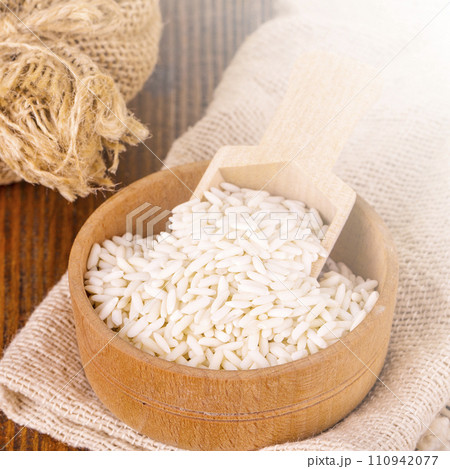 White uncooked Thailand jasmine rice in small burlap bag with wooden spoon on wood tablle on sunlight 110942077