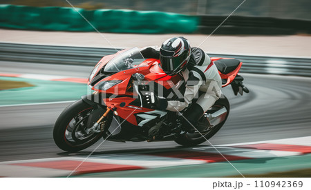 Racing motorbike rider in helmet and gear racing at high speed on race track with motion blur Racing motorbike rider in helmet and gear racing at high speed on race track with motion blur 110942369