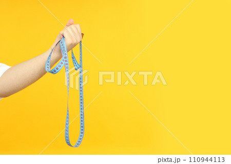 Tape measuring body parameters, in a man's hand, on a yellow background. Tape measuring body parameters, in a man's hand, on a yellow background. 110944113