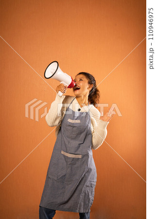 Asian girl wearing an apron screaming into a megaphone Asian girl wearing an apron screaming into a megaphone 110946975