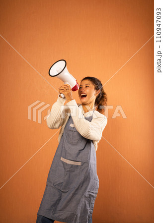 Asian girl wearing apron using megaphone with both hands Asian girl wearing apron using megaphone with both hands 110947093