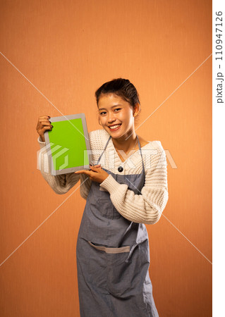 Attractive Asian girl wearing apron holding blank digital tablet Attractive Asian girl wearing apron holding blank digital tablet 110947126