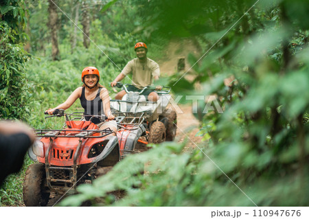 happy asian couple riding the atv together spending their holiday 110947676