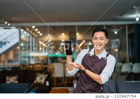 male shop assistant with hand gesture presenting mobile phone in furniture store 110947754