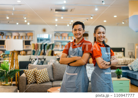 two smiling shop assistants with crossed arms standing in a furniture store 110947777