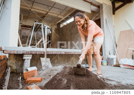 Asian woman mixing cement and sand using a hoe Asian woman mixing cement and sand using a hoe 110947805