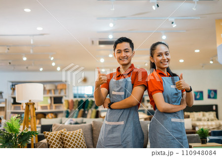 a couple of shop assistants with thumbs up in a furniture store a couple of shop assistants with thumbs up in a furniture store 110948084