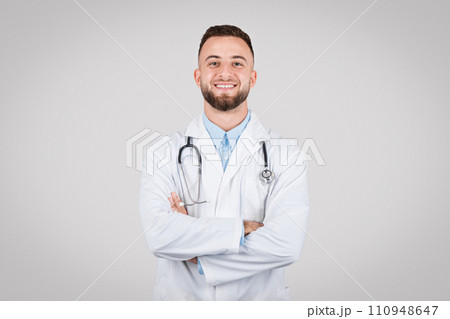 Confident young doctor posing with arms crossed and stethoscope around his neck against grey background Confident young doctor posing with arms crossed and stethoscope around his neck against grey background 110948647