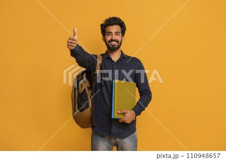 Happy indian student guy with backpack and notebooks showing thumbs up gesture 110948657