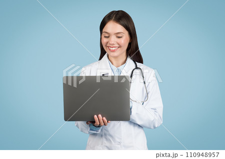 Happy female doctor with laptop on blue background 110948957