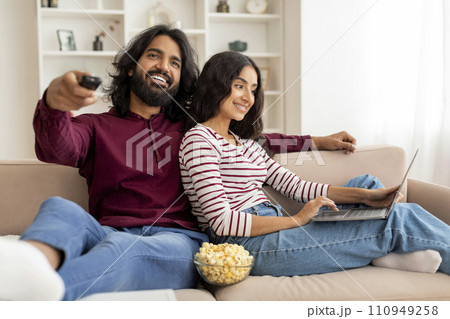 Relaxed millennial couple chilling at home, watching tv, using laptop 110949258