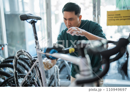 young man cleaning bicycle with foaming soap with indoor background young man cleaning bicycle with foaming soap with indoor background 110949697