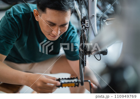 handsome young man repairing bicycle pedal with allens key in bicycle shop handsome young man repairing bicycle pedal with allens key in bicycle shop 110949769