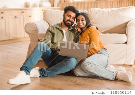 Happy hindu couple with laptop relaxing on living room floor Happy hindu couple with laptop relaxing on living room floor 110950114