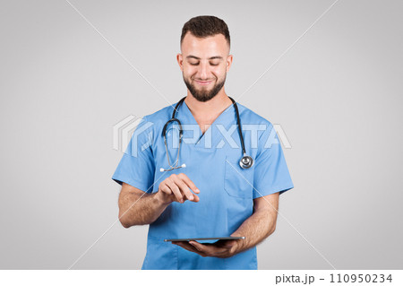 Doctor man in blue uniform using tablet and smiling on grey background 110950234