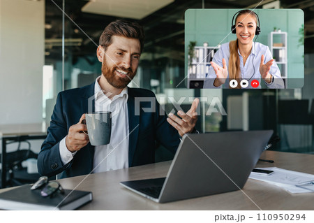 Handsome positive caucasian businessman talking with business partners via laptop Handsome positive caucasian businessman talking with business partners via laptop 110950294