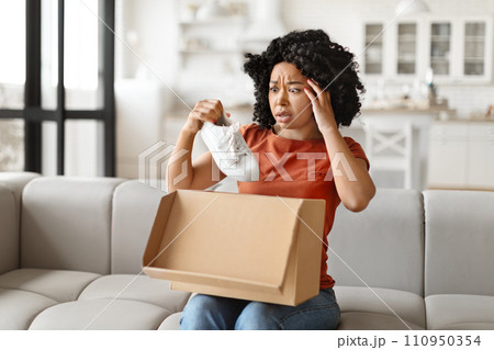 Wrong Parcel. Anxious black woman taking shoes out of box at home Wrong Parcel. Anxious black woman taking shoes out of box at home 110950354