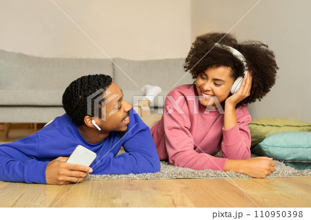 Black couple enjoys music online through headphones and cellphone indoor Black couple enjoys music online through headphones and cellphone indoor 110950398