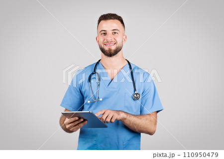Male doctor in blue with stethoscope using tablet, grey background 110950479