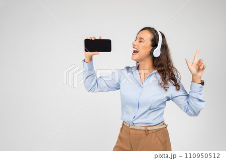 Glad european millennial woman in wireless headphones with open mouth, listen music, sing song at phone 110950512