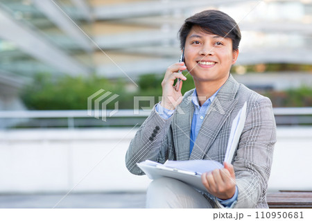 Asian man engages in business talk on cellphone against cityscape 110950681
