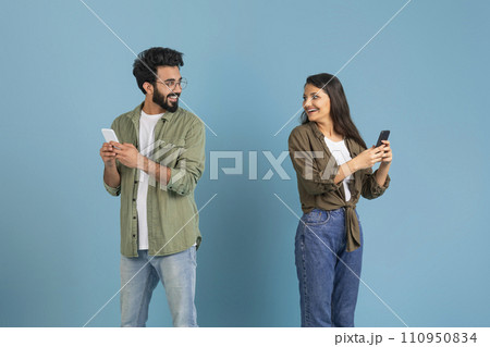 Man and woman using phones and looking at each other Man and woman using phones and looking at each other 110950834