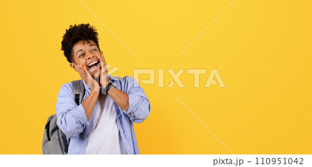 Excited black male student with backpack on yellow background looking at free space 110951042