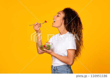 Young black woman in casual enjoying tasty veggie salad, studio 110951186