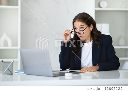 Shocked businesswoman sitting at office, looking at laptop screen 110951294