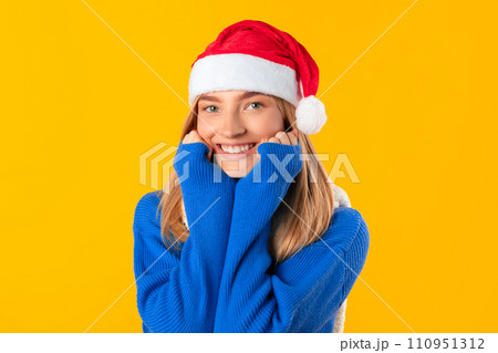 Cheerful woman in Santa hat and blue sweater on sunny yellow background. Cheerful woman in Santa hat and blue sweater on sunny yellow background. 110951312