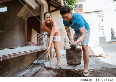 husband uses a hoe to make cement mixture and wife helps 110951338