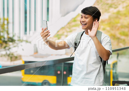 Positive asian guy travel blogger taking selfie by phone Positive asian guy travel blogger taking selfie by phone 110951348