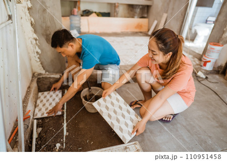 young Asian couple tiling together while renovating their own home young Asian couple tiling together while renovating their own home 110951458