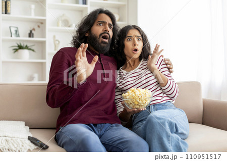 Scared young indian couple watching horror movie on TV Scared young indian couple watching horror movie on TV 110951517