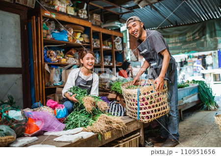 male seller lifting basket and helping partner arranging vegetables 110951656
