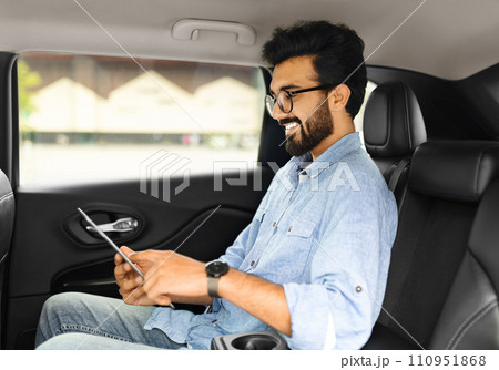 Cheerful eastern guy using digital tablet while sitting in taxi 110951868