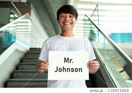 Cheerful millennial asian guy holding placard with name 110951909