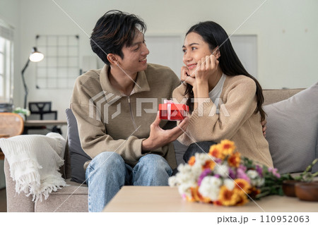 Romantic young asian couple embracing giving present in living room at home. Fall in love. Valentine concept Romantic young asian couple embracing giving present in living room at home. Fall in love. Valentine concept 110952063