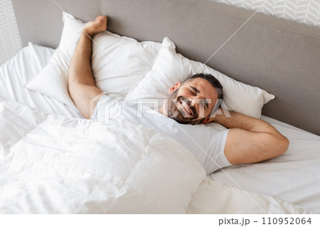 man stretching his arms wakes up on cozy bed indoor man stretching his arms wakes up on cozy bed indoor 110952064