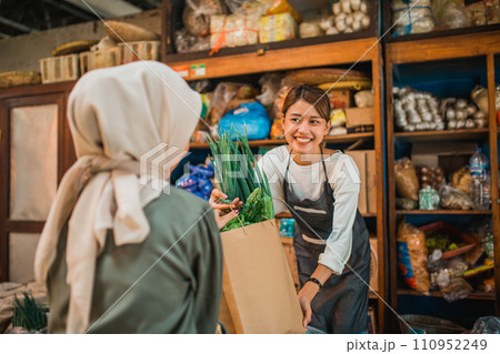 female greengrocery seller giving customer fresh vegetables 110952249