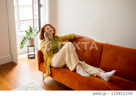 Happy Senior Woman Talking On Cellphone While Relaxing On Couch At Home, Happy Senior Woman Talking On Cellphone While Relaxing On Couch At Home, 110952250