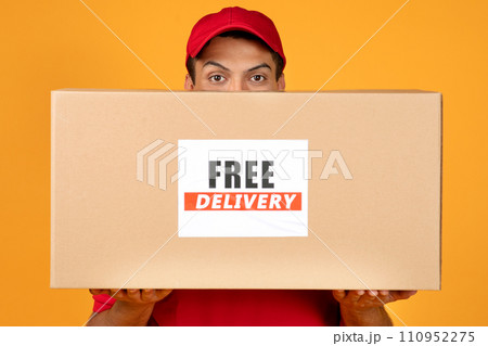 deliveryman peeking from cardboard box with Free Delivery label, studio 110952275