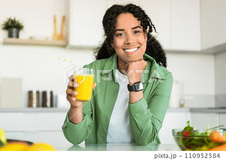 black woman holds glass of orange juice in her kitchen 110952584