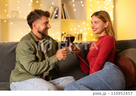 Happy couple toasting with wine glasses in a cozy room Happy couple toasting with wine glasses in a cozy room 110952857