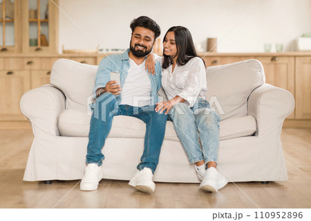 Loving young indian couple with smartphone on the couch 110952896