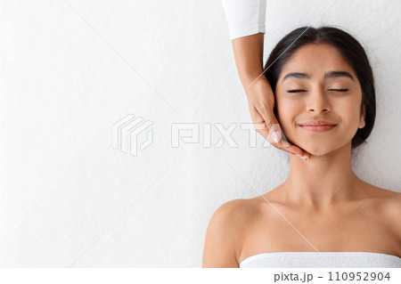 Joyful young indian woman relaxing during face lifting massage 110952904