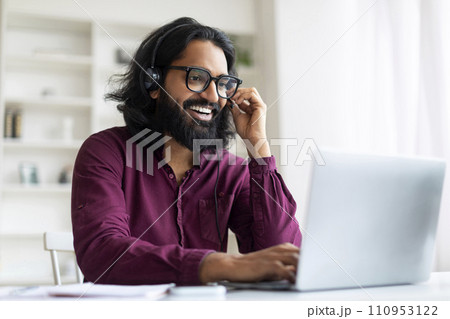 Handsome Young Indian Man Wearing Headset And Eyeglasses Watching Webinar On Laptop 110953122