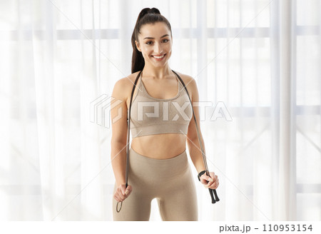 Beautiful well-fit brunette sportswoman posing with skipping rope indoors 110953154